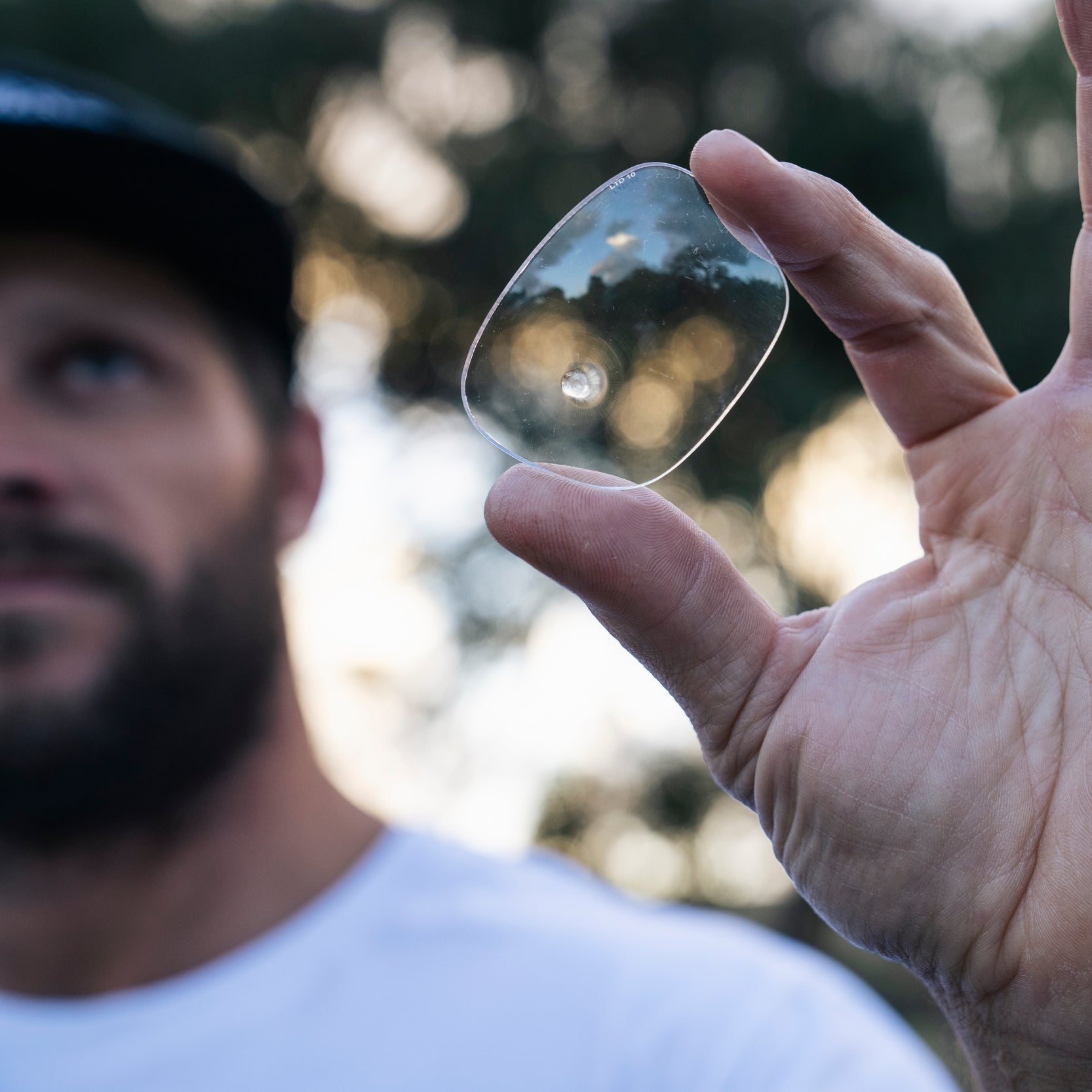 Hand holding a clear,sunglass lens with a blurred natural background
